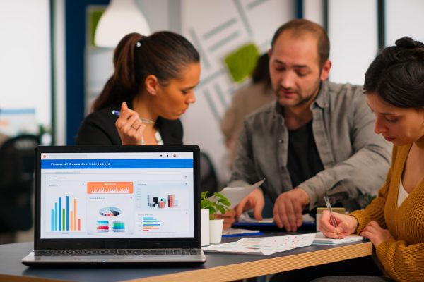 Business woman talking about financial project, taking notes, discussing start up ideas using laptop. Diverse employees gathered in co-working, working process in busy company, teamwork help concept